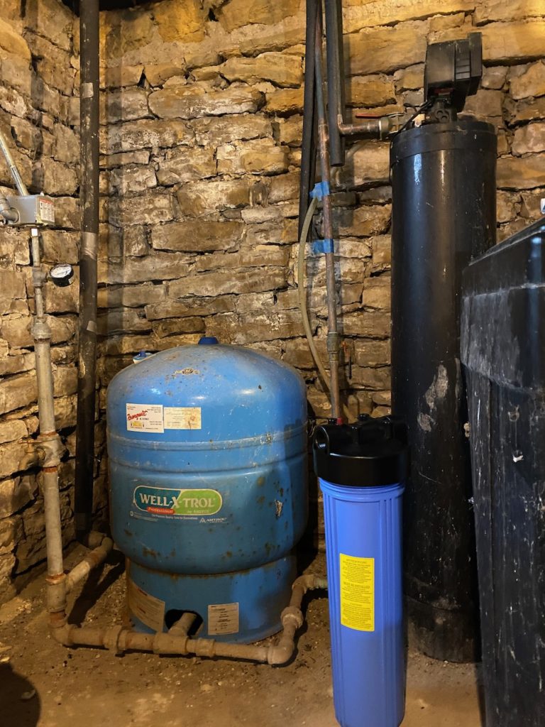A water pressure tank and filter sitting in a limestone basement