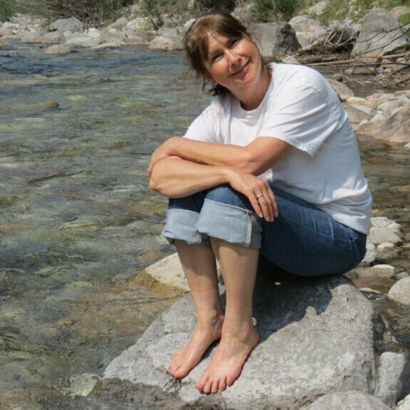 Author of memoir and adventure stories lounges in t-shirt and jeans by the stream.